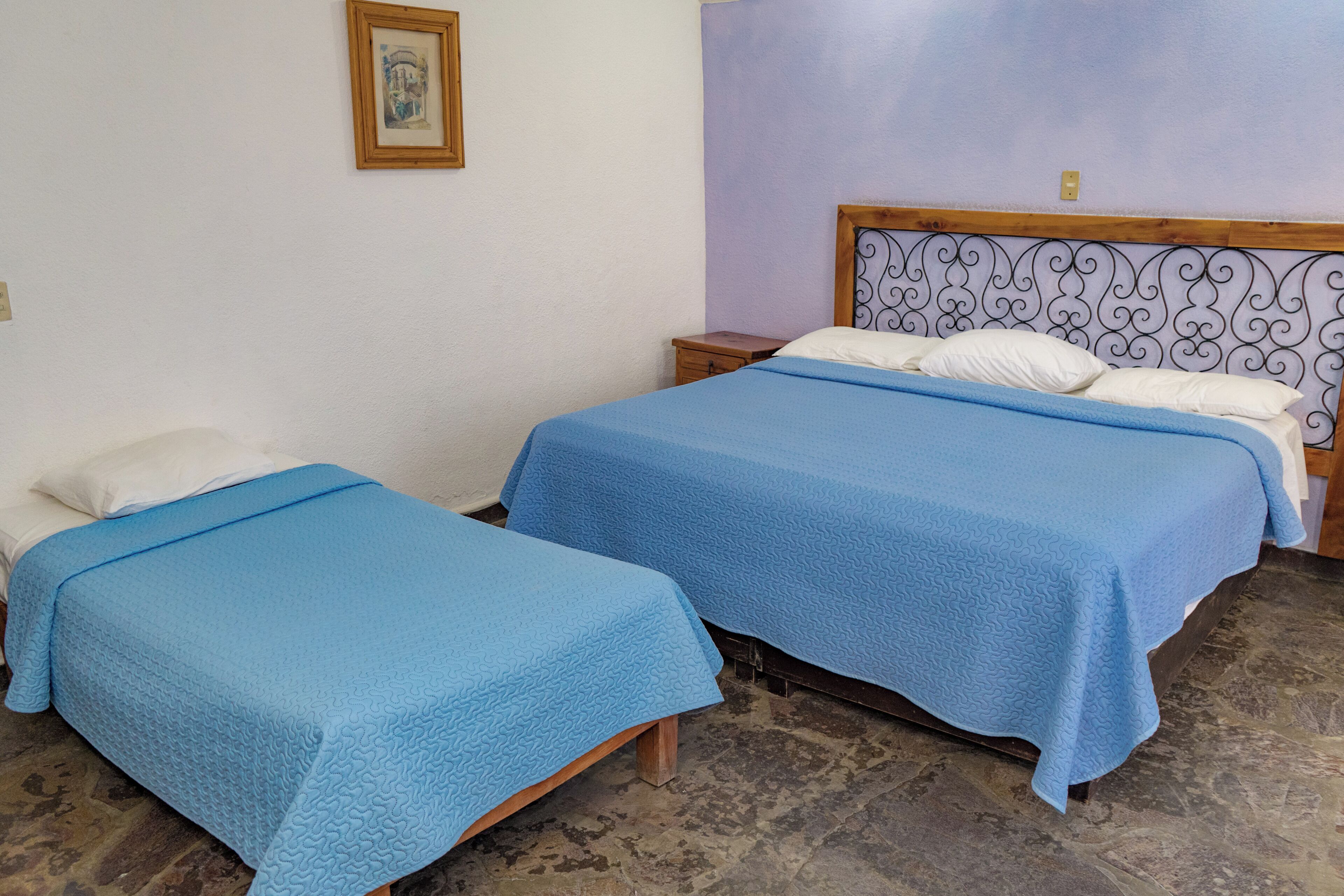 Zwei Einzelbetten mit blauer Bettwäsche, ein Holz-Kopfteil, ein kleiner Nachttisch und ein an der Wand hängendes Bild.