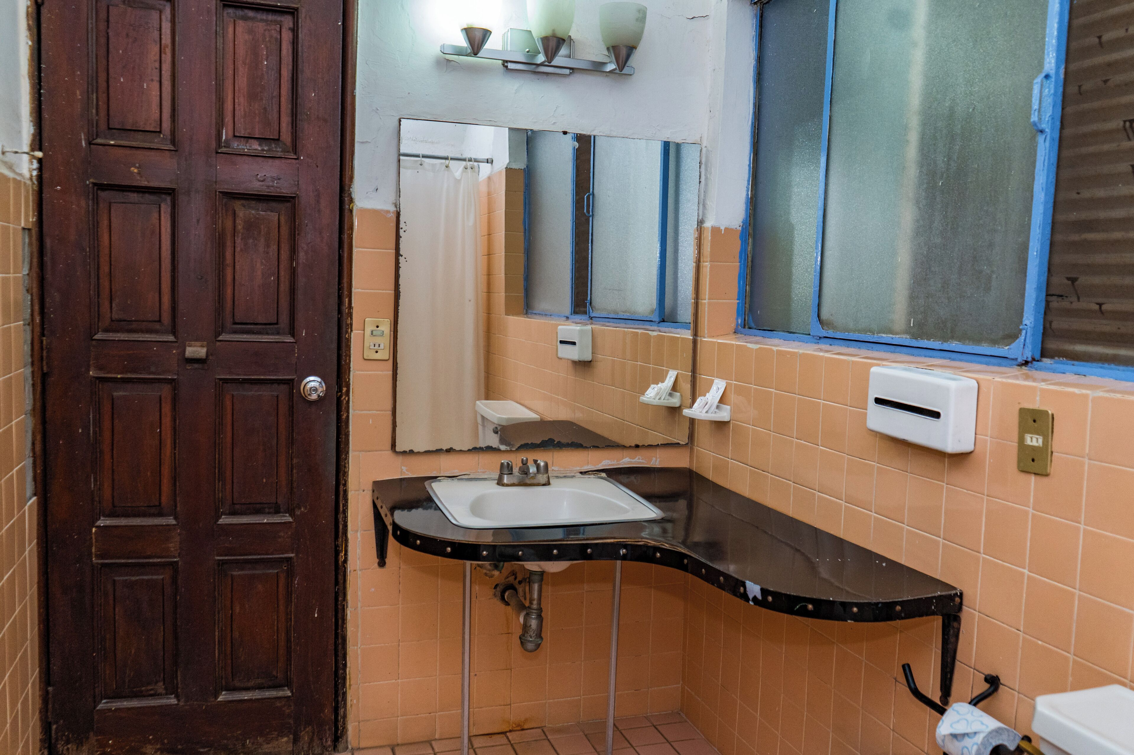 A bathroom with a wooden door, a sink with a mirror, and a window with a blue frame.