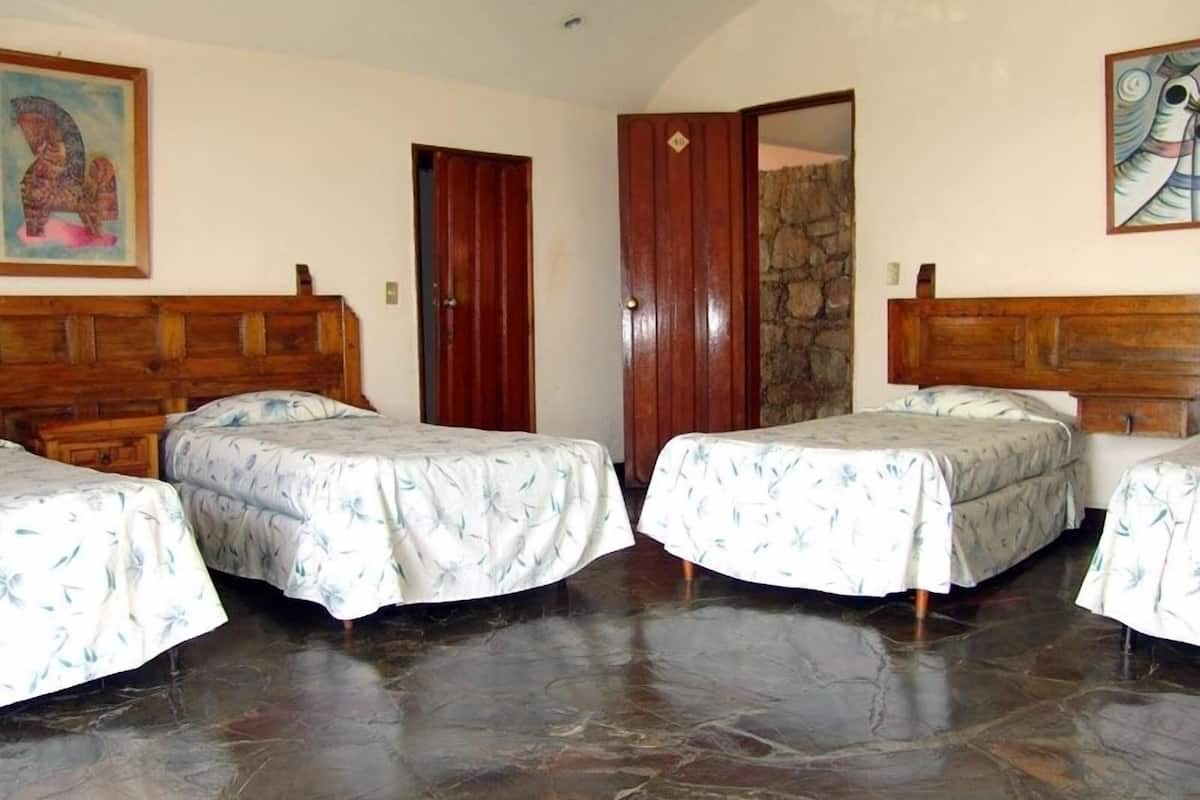 Una habitación con cuatro camas, cabeceros de madera, una pared de piedra y una puerta.