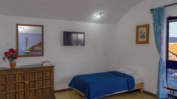 A bedroom with a bed, a dresser, a television, a window with curtains, and a painting on the wall.