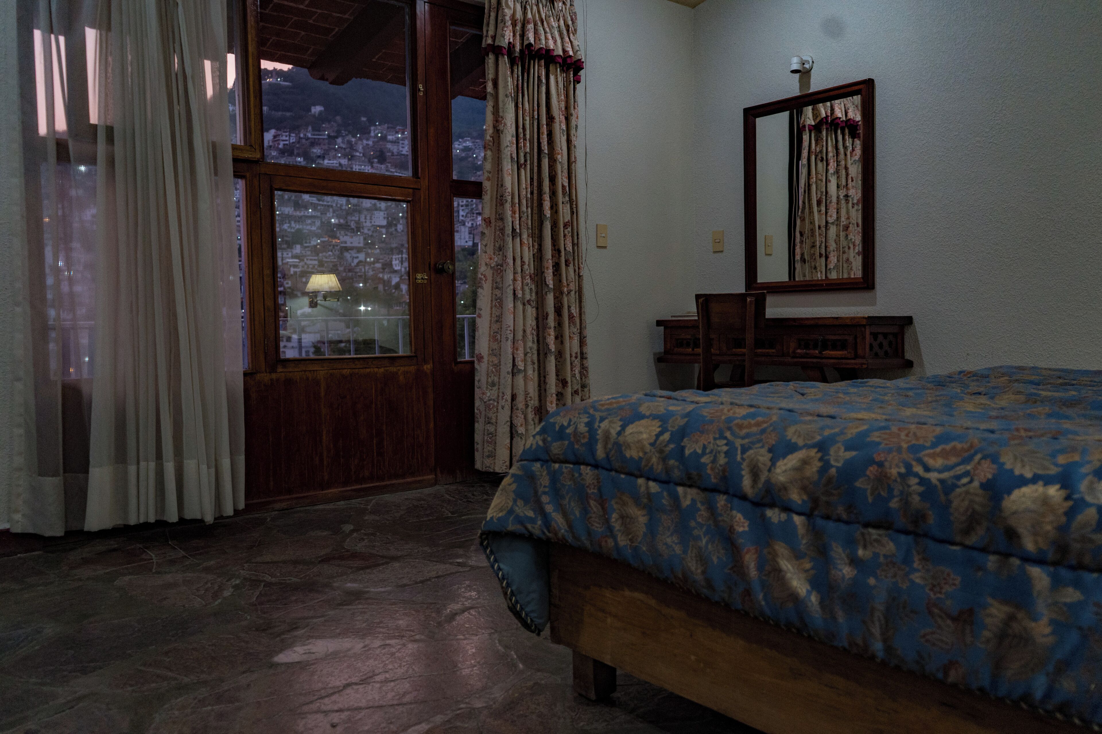 Un dormitorio con cama, cómoda de madera, espejo y ventana con cortinas.