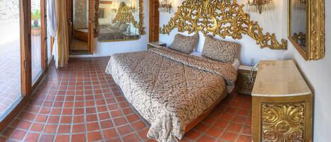 A bedroom with a large bed, ornate wall mirrors, and a tiled floor.