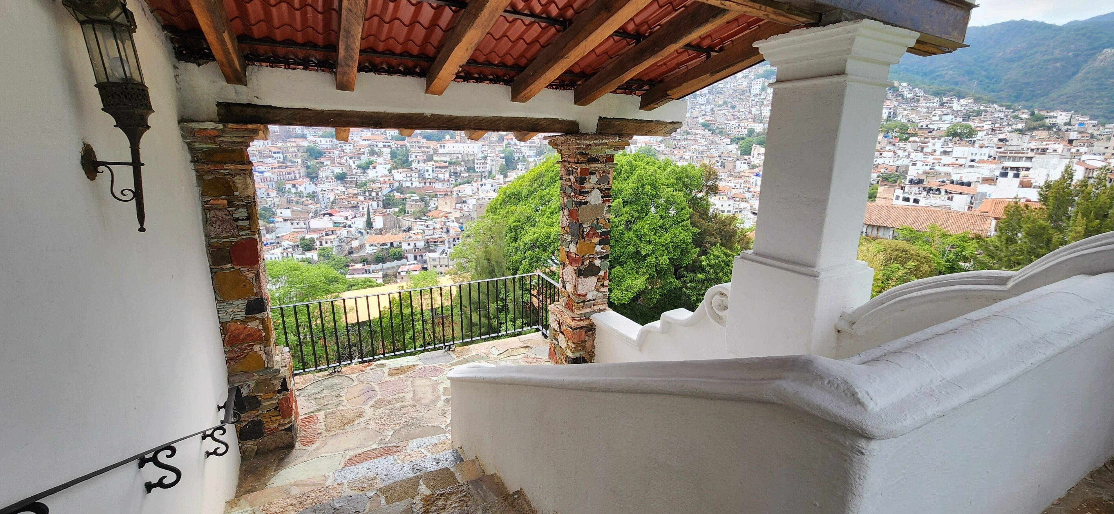 Un balcón con suelo de piedra, paredes blancas y vista a una ciudad densamente poblada.