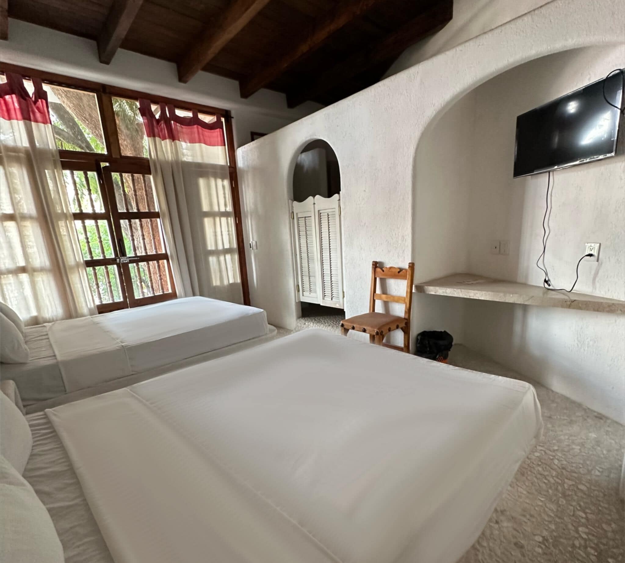 Una habitación con dos camas, un televisor montado en la pared y una ventana con cortinas.