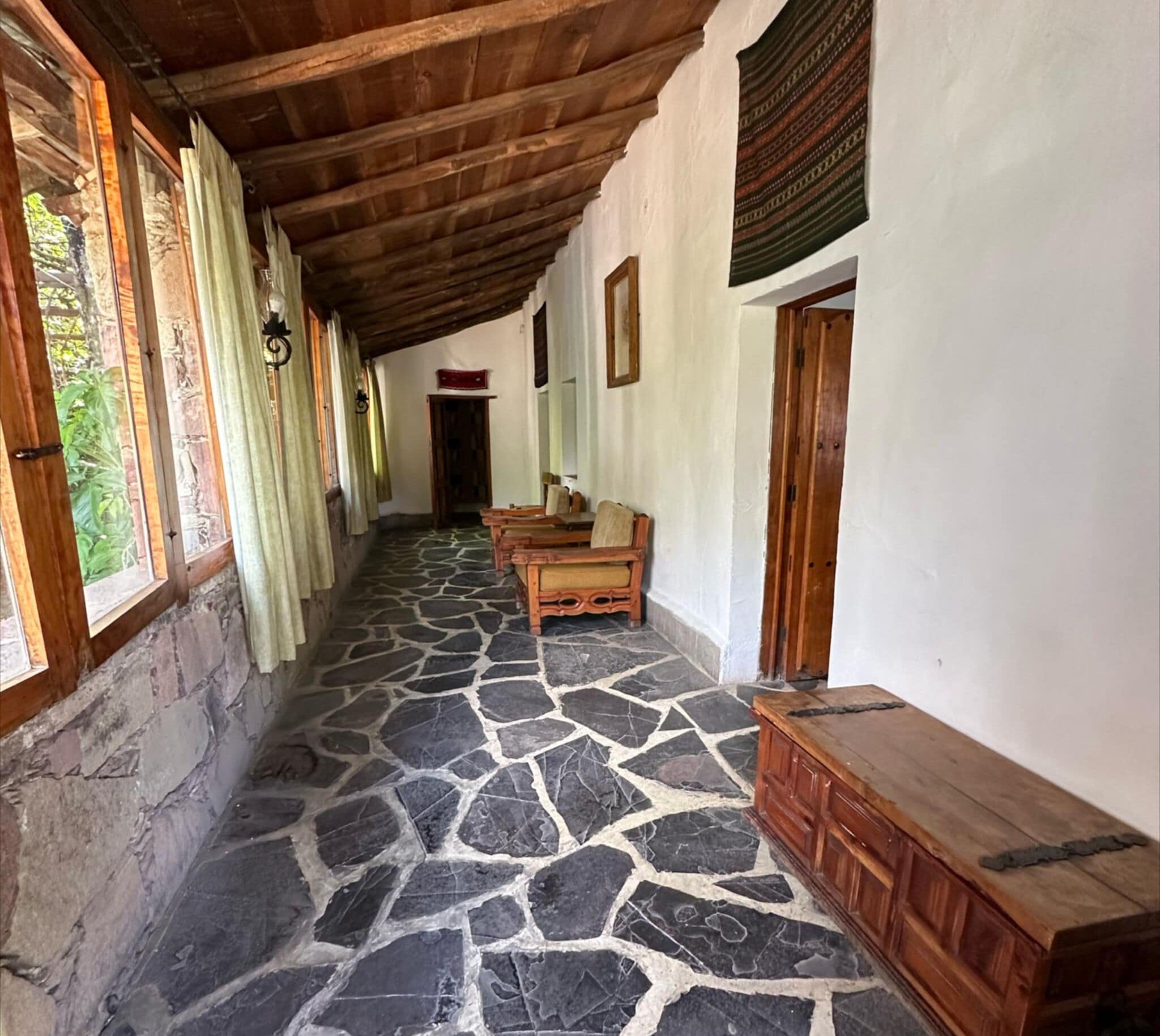 A corridor with stone flooring, wooden benches, and a wooden bench with a cushion.