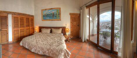 Un dormitorio con una cama grande, persianas de madera, un cuadro y un balcón con vistas.