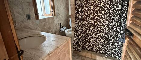 A bathroom with a large bathtub, a toilet, and a shower curtain with a swirling pattern.
