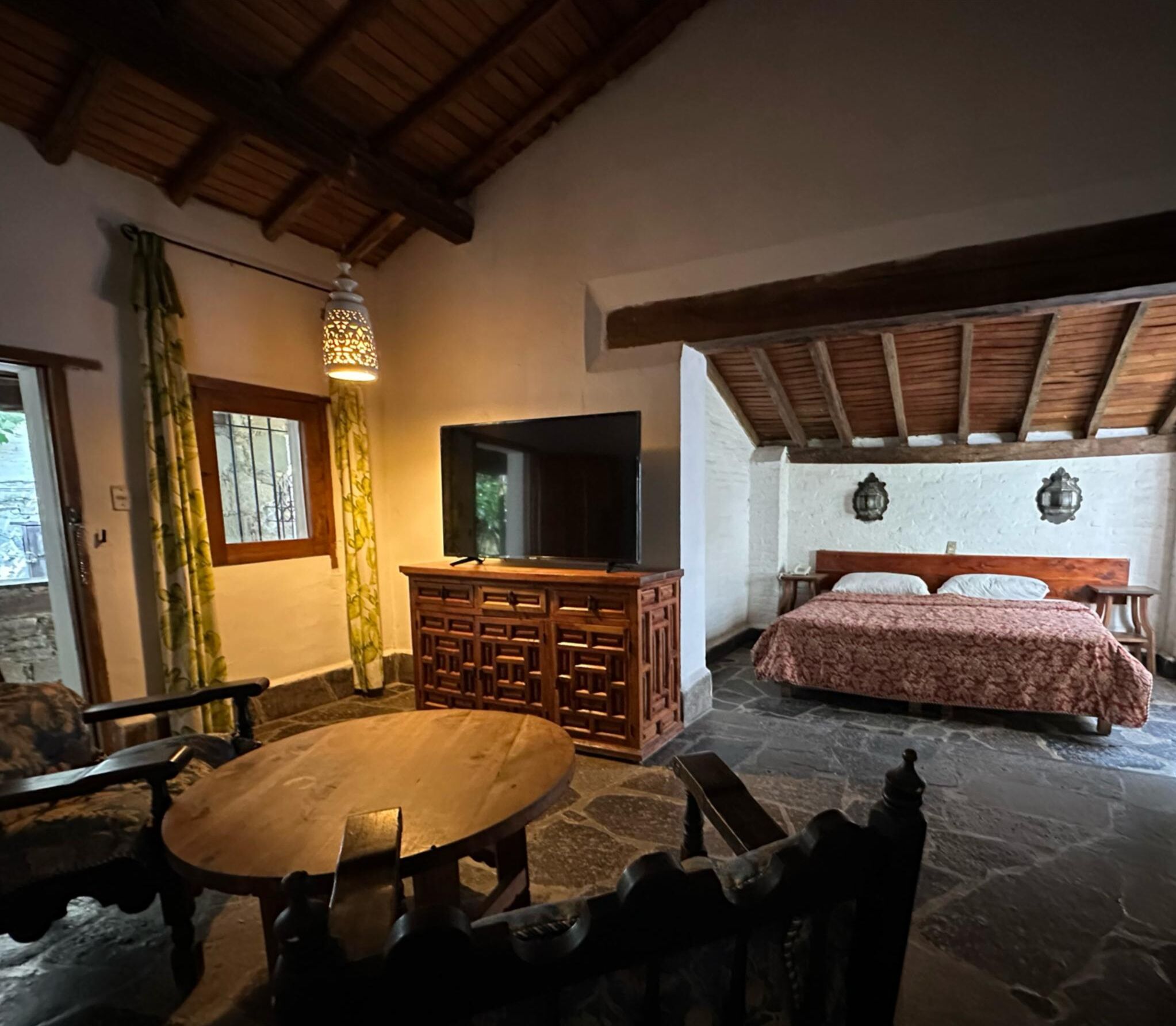 A cozy room with a bed, a TV, a wooden table, and a stone floor.