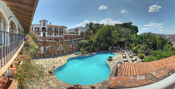 A swimming pool surrounded by a garden with a tiled floor, a white building with arches, and a view of a hill with trees. - Hotel-Museo Posada de la Misón (Taxco)