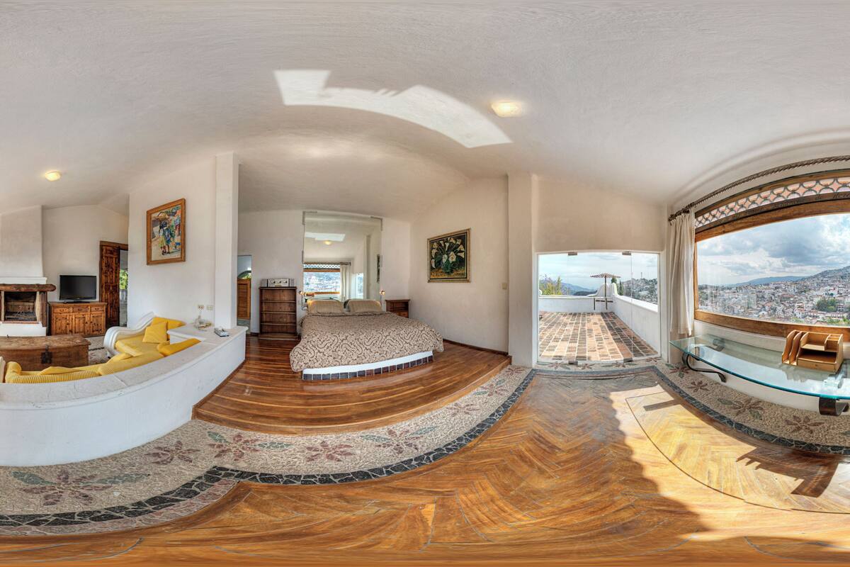 Ein großzügiger Wohnraum mit einem gebogenen weißen Sofa, einem Glastisch und Blick auf eine Stadtlandschaft durch große Fenster.