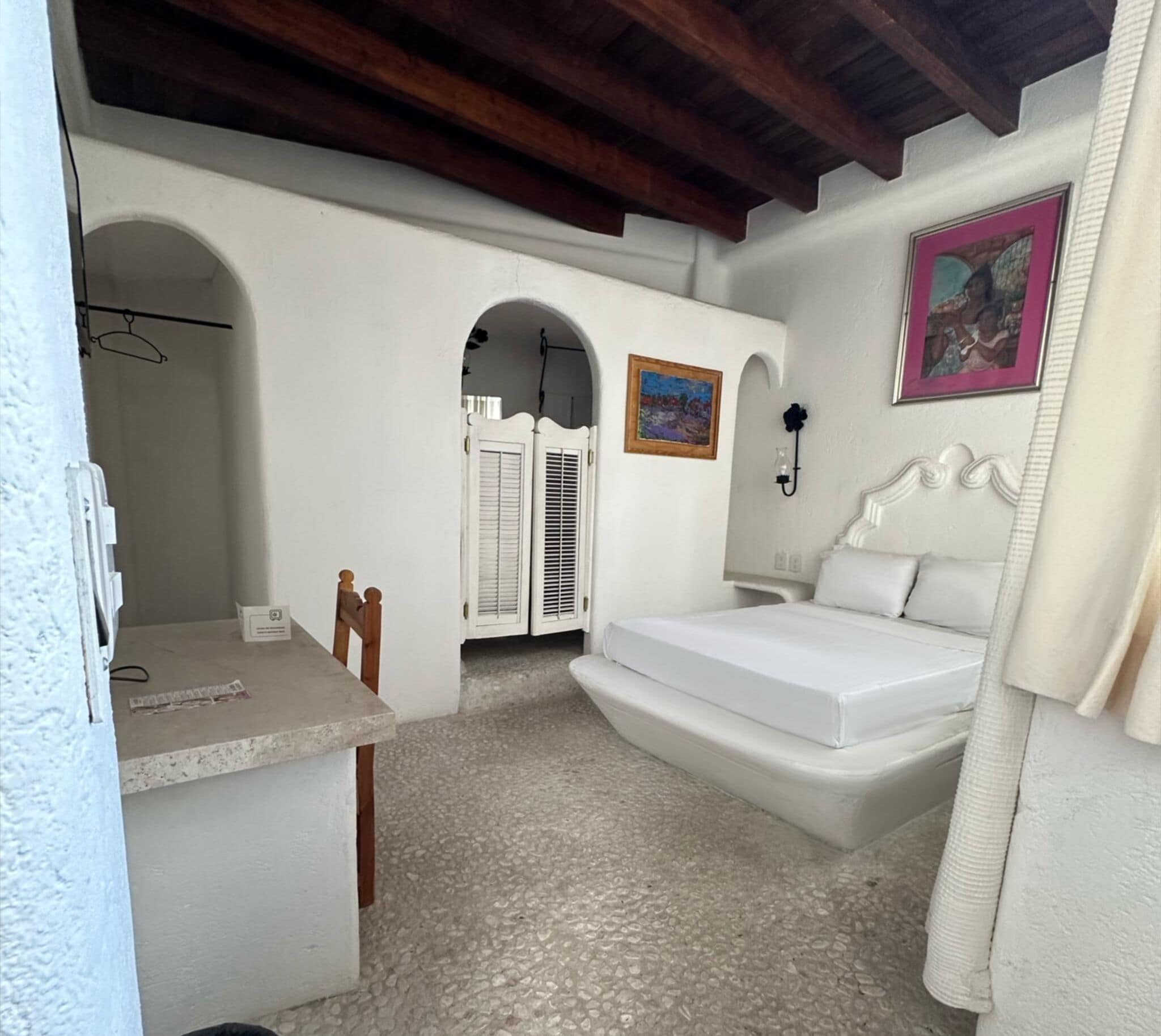 Ein Schlafzimmer mit einem Bett, einem Schreibtisch und einem Sessel. Es gibt zwei Türen und ein Fenster.