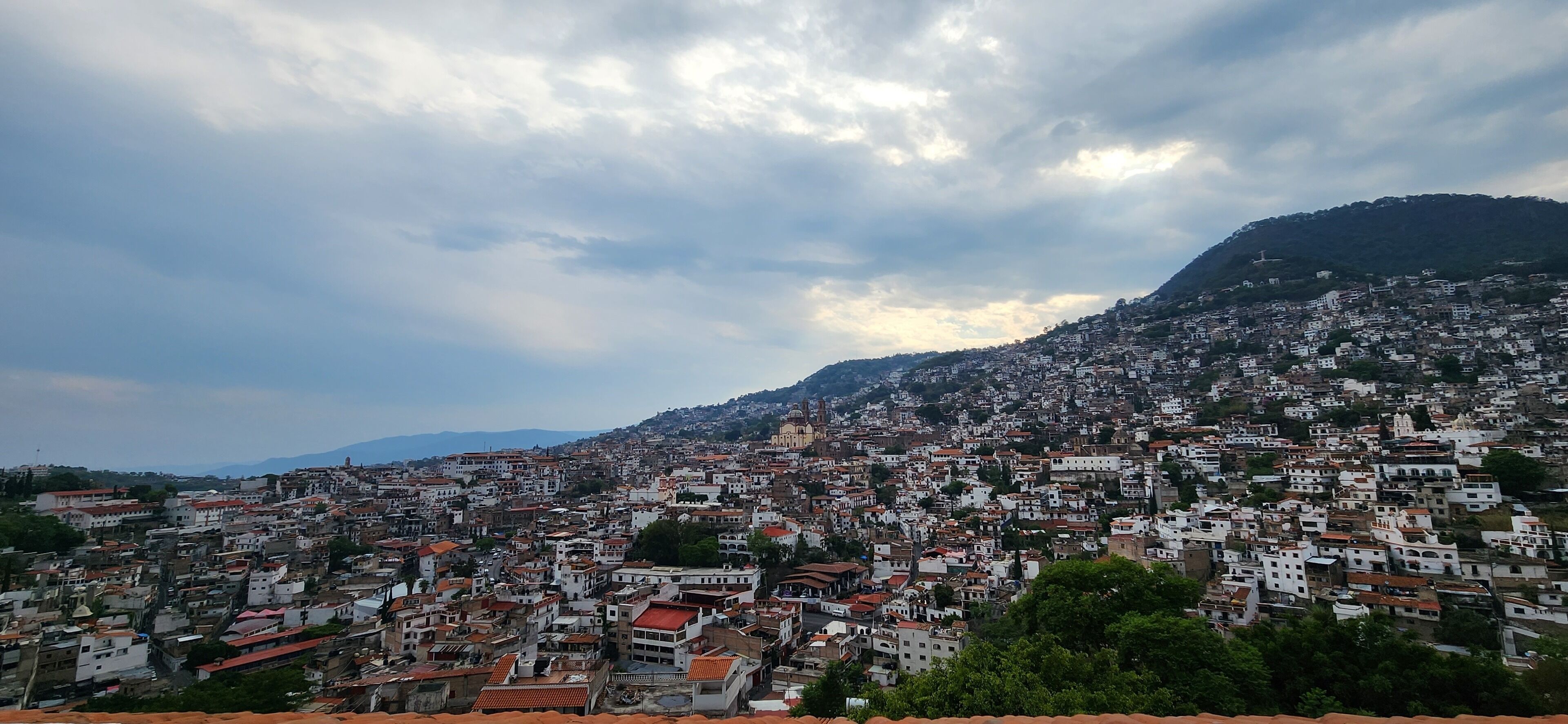 A densely packed urban area with buildings closely situated on a hillside, under a cloudy sky.