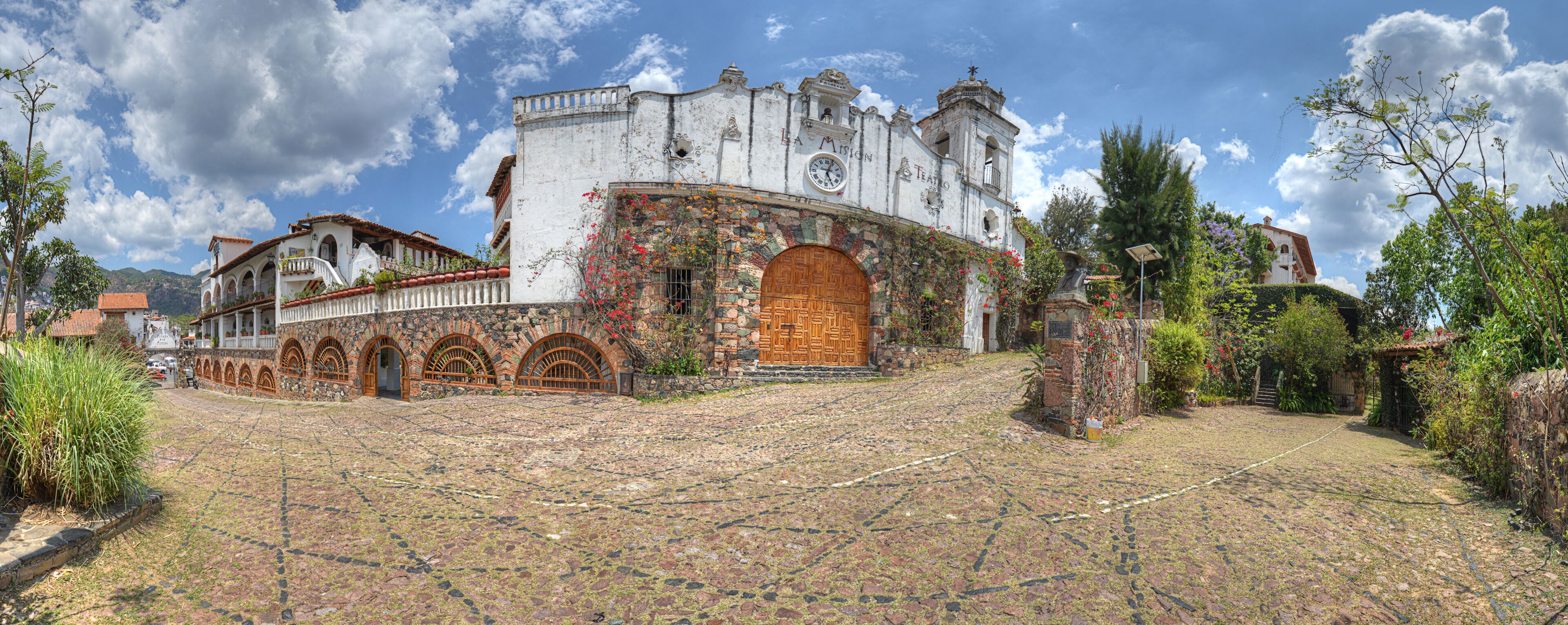 Un edificio storico con una torre dell'orologio, finestre ad arco e un cortile in pietra.