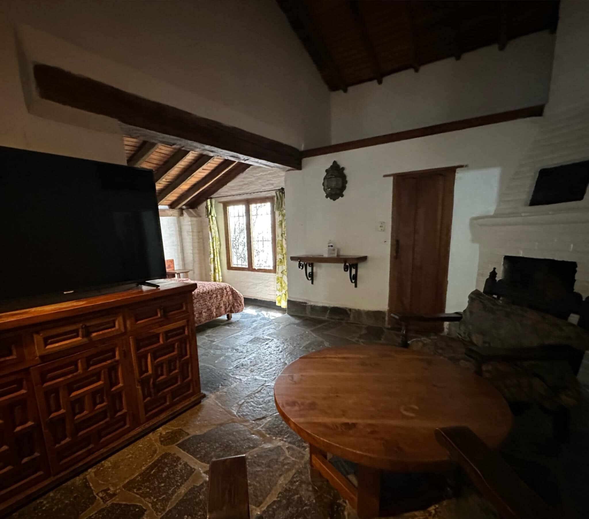 Una sala de estar rústica con piso de piedra, muebles de madera, chimenea y un televisor sobre un mueble de madera.