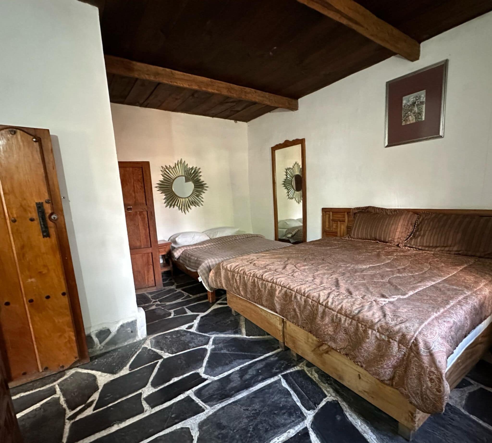 Ein Schlafzimmer mit einem großen Bett, einem Holzschrank, Steinböden und einem Holzbalken an der Decke.