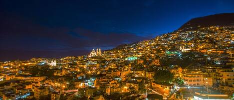 A densely packed urban area at night with illuminated buildings and a prominent hill with a structure on top.