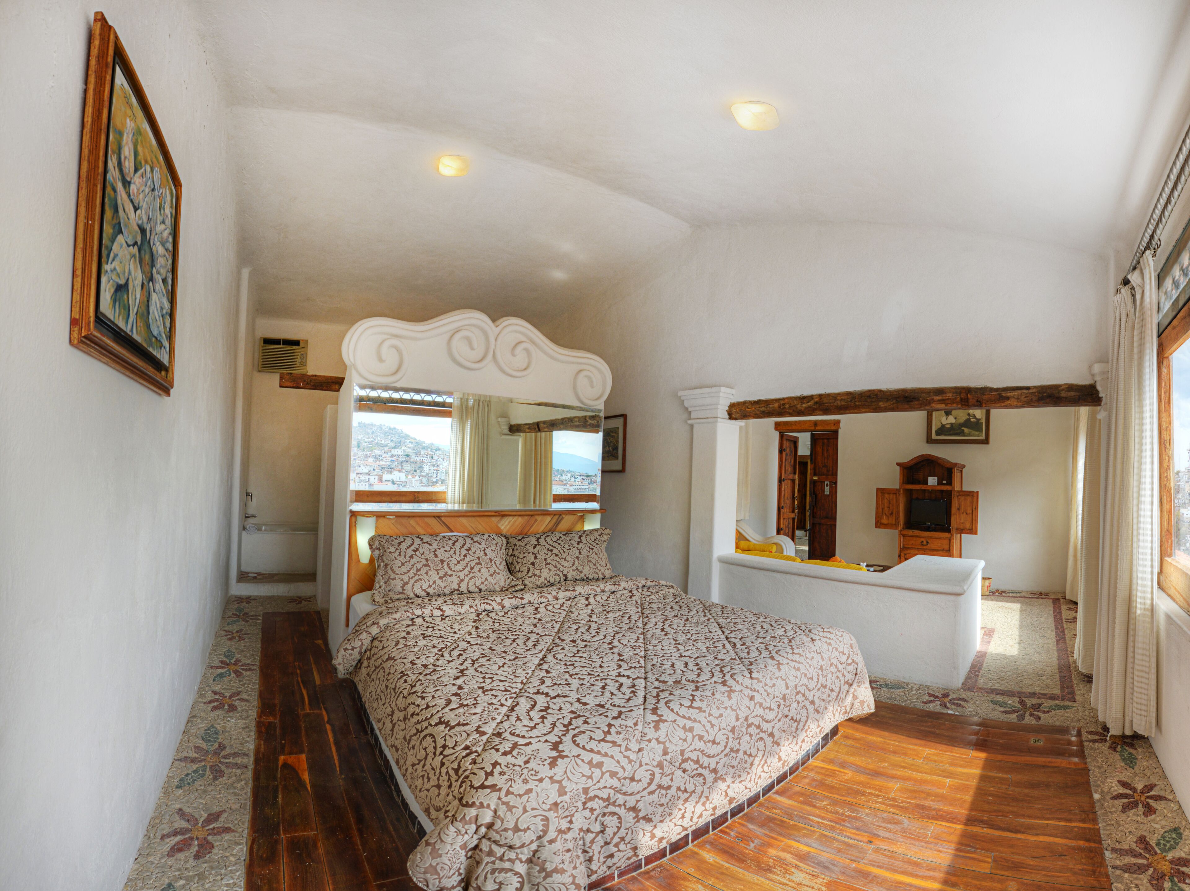 Un dormitorio con una cama grande, un aparador de madera, un espejo y una ventana con vistas.