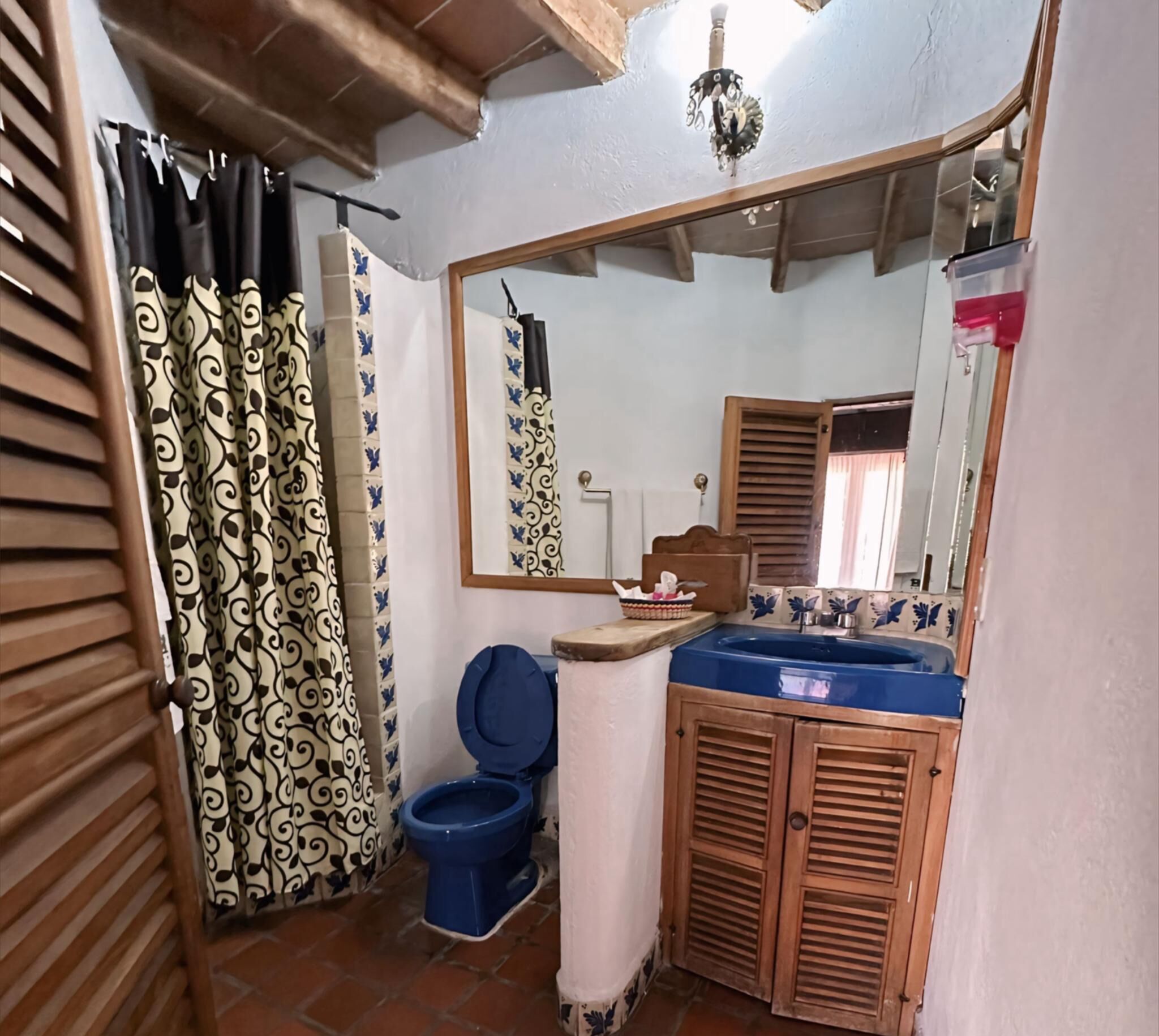 A bathroom with a blue toilet, a sink with a mirror above it, and a shower curtain with a black and white pattern.