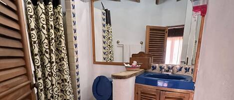 A bathroom with a blue toilet, a sink with a mirror above it, and a shower curtain with a black and white pattern.