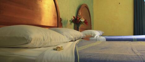 A double bed with white and blue bedding, a wooden headboard, and a vase with flowers on the nightstand.