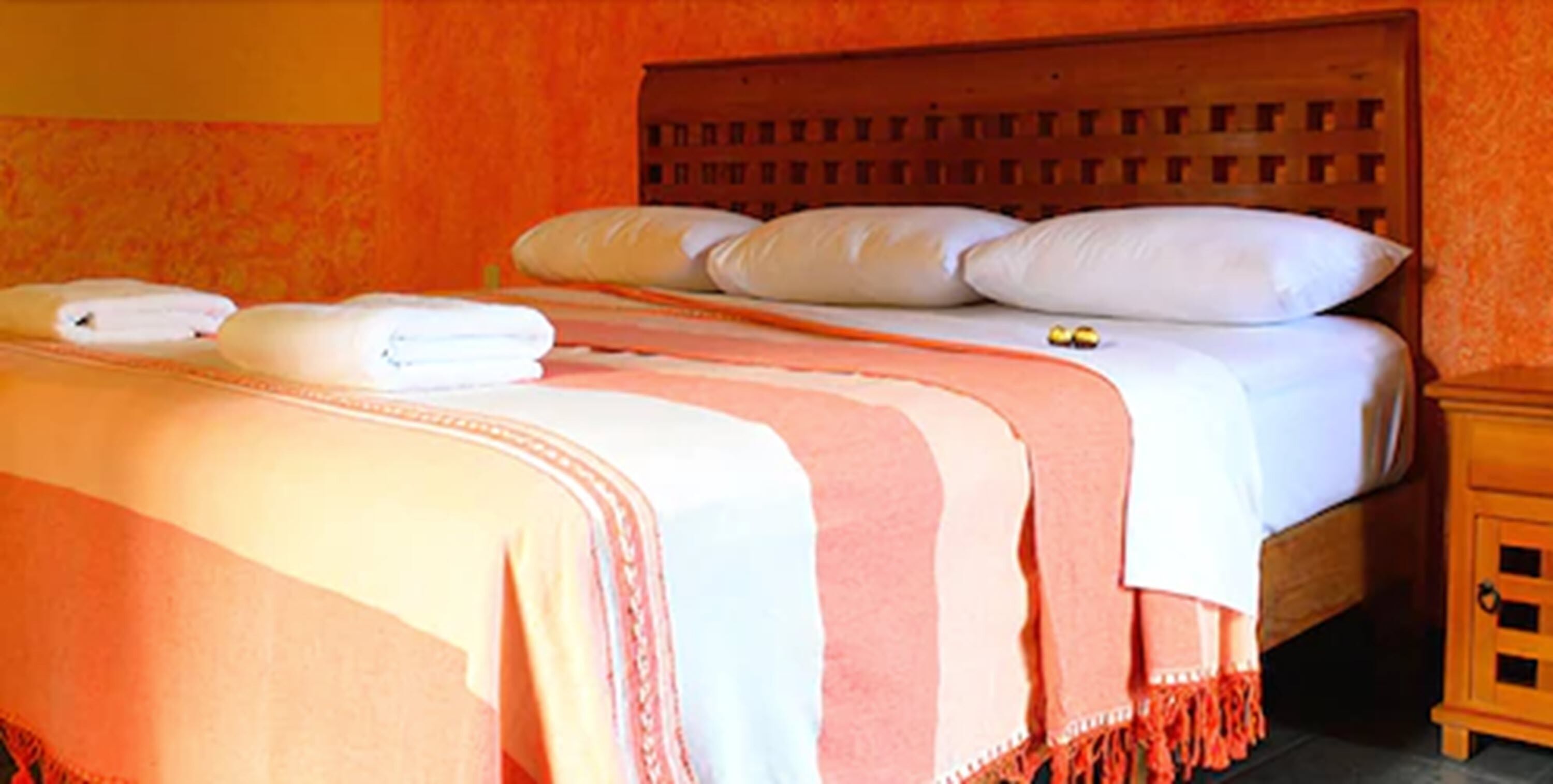 A neatly made bed with white and pink bedding, a wooden headboard, and a small wooden nightstand with a drawer.