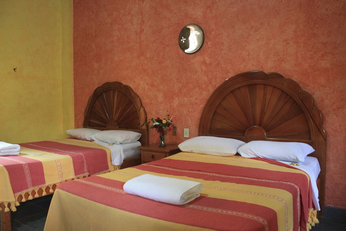 Una habitación de hotel con dos camas individuales, cada una con cabecero de madera, una mesita de noche con un florero y un reloj de pared.