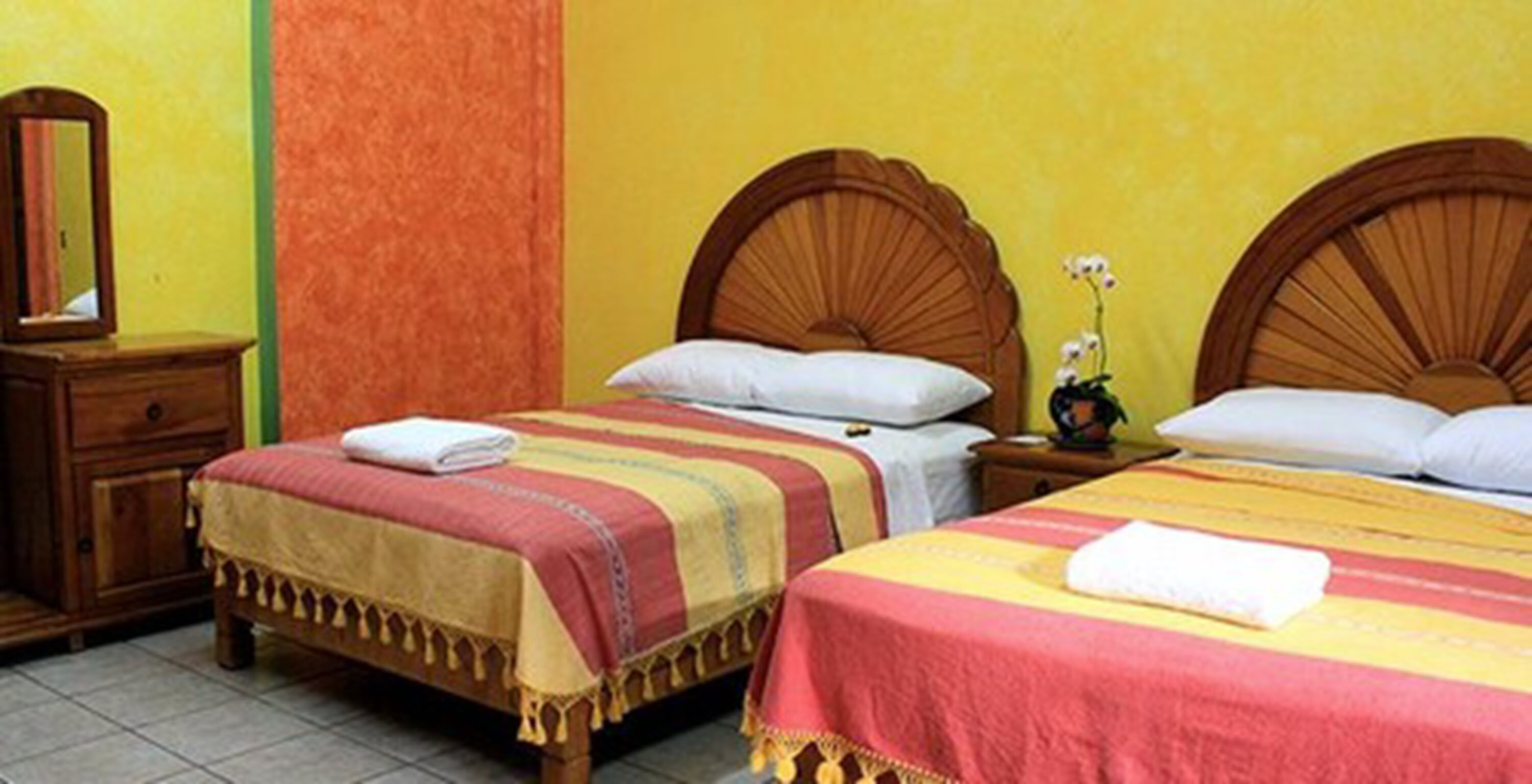 A hotel room with two single beds, wooden headboards, and a nightstand with a mirror.