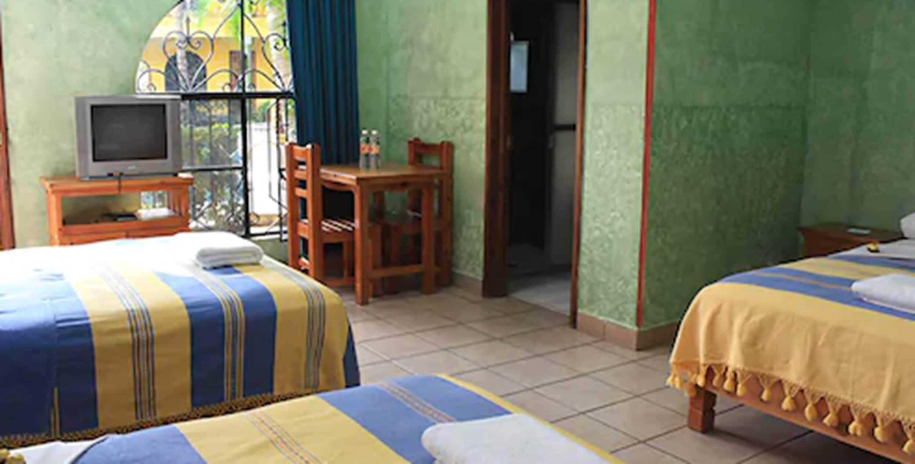 Ein Hotelzimmer mit zwei Betten, einem Fernseher auf einem kleinen Tisch, einem Sessel und Blick durch ein Fenster.