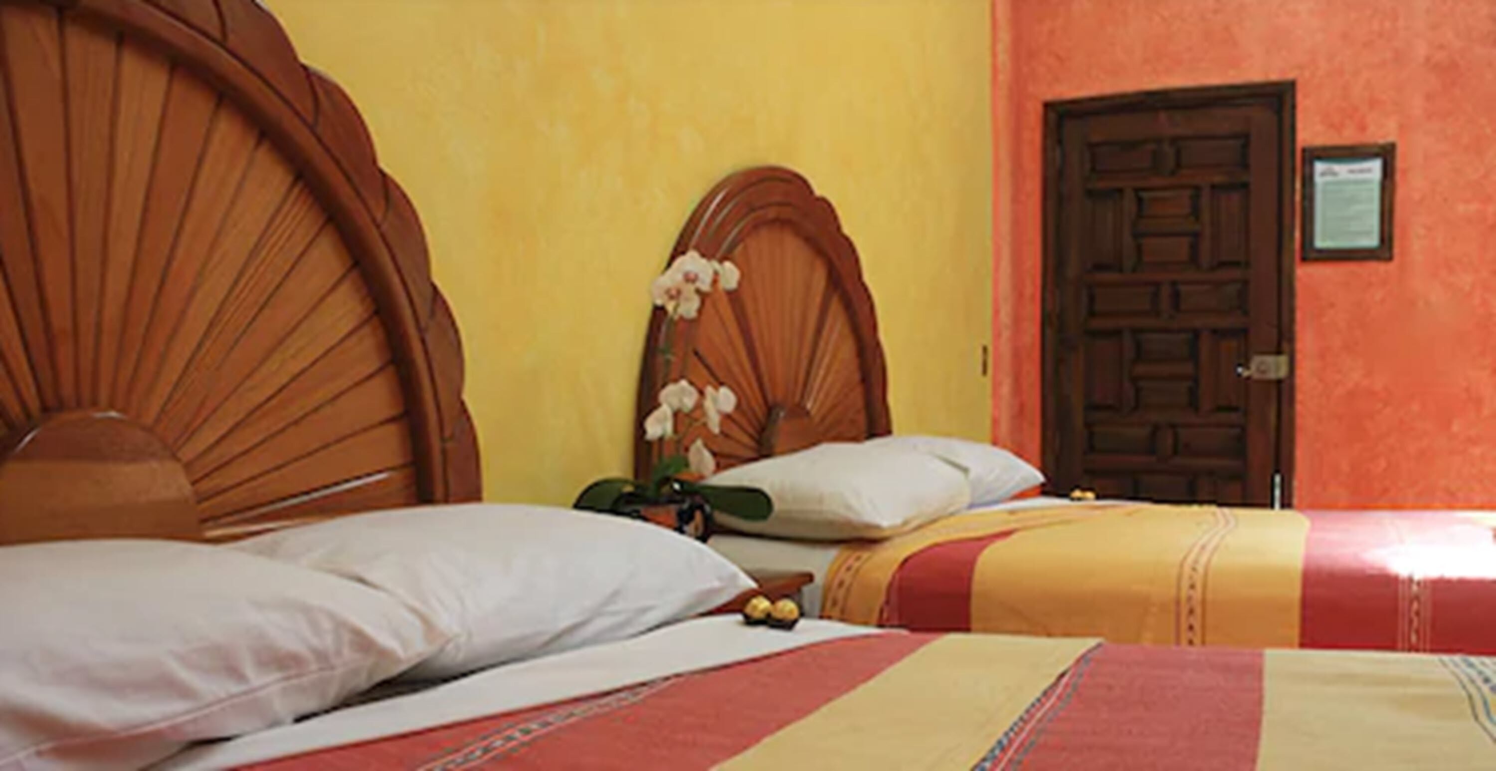 Quarto de hotel com duas camas e cabeceiras de madeira, e uma porta.