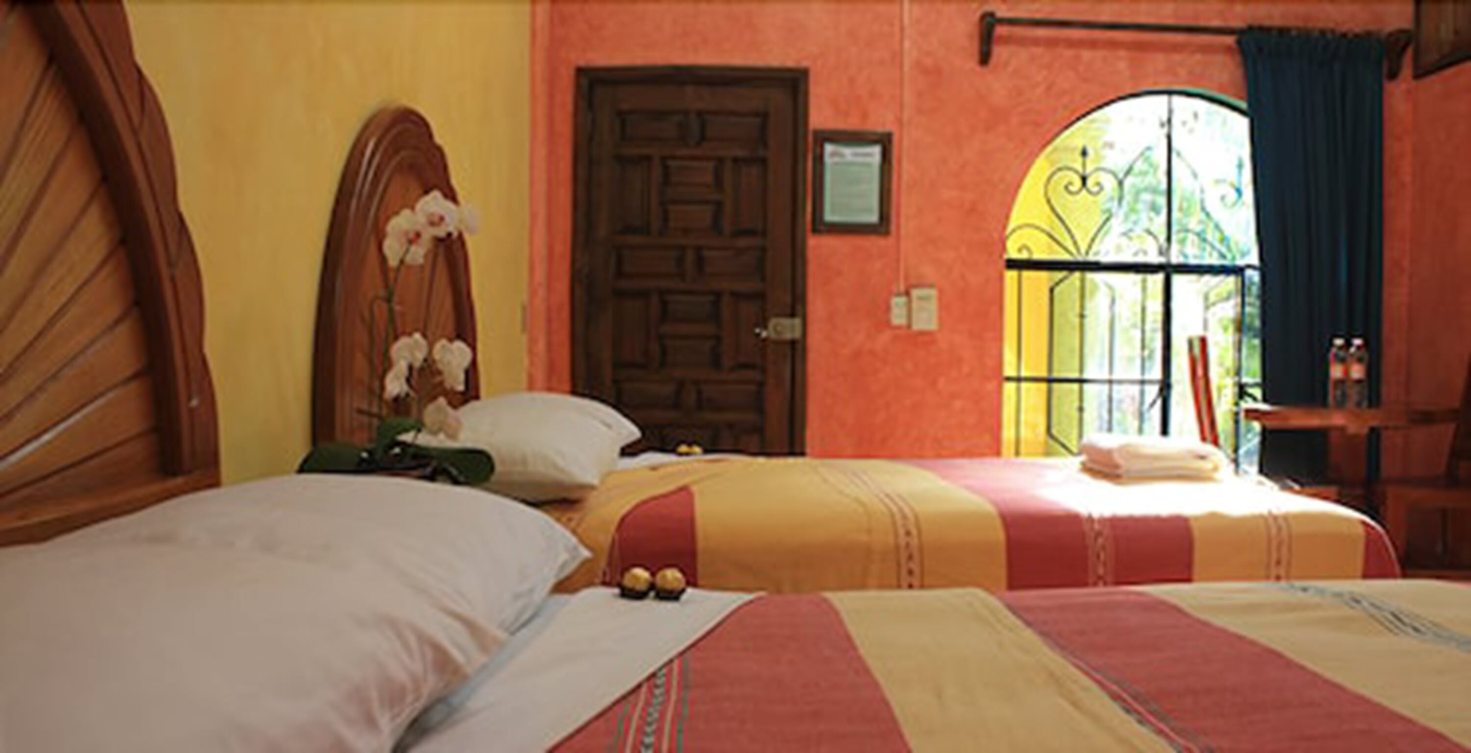 A hotel room with two beds, a wooden headboard, a door, and a window with a decorative iron grille.