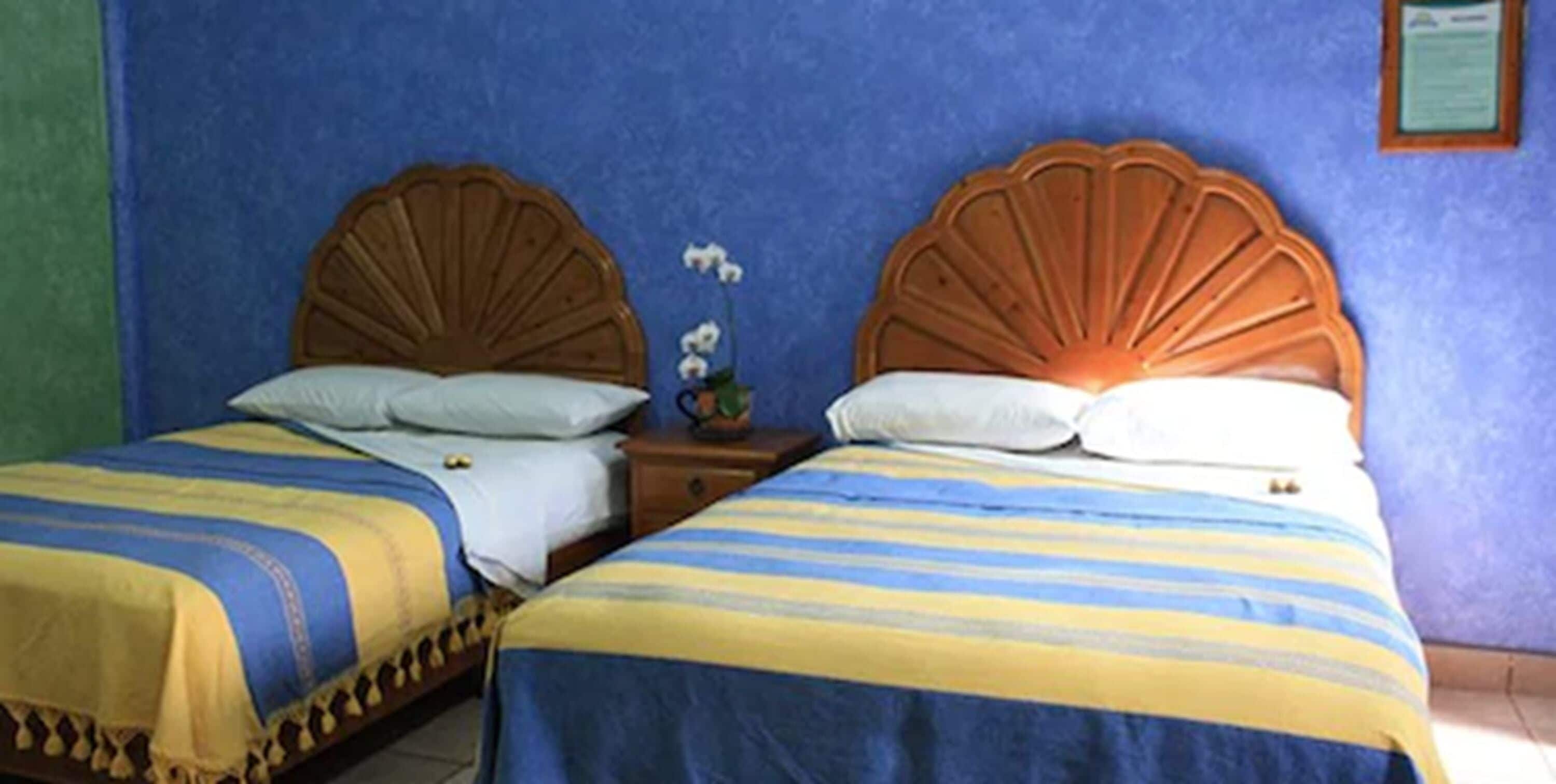 A room with two beds, each with a wooden headboard and striped bedding.