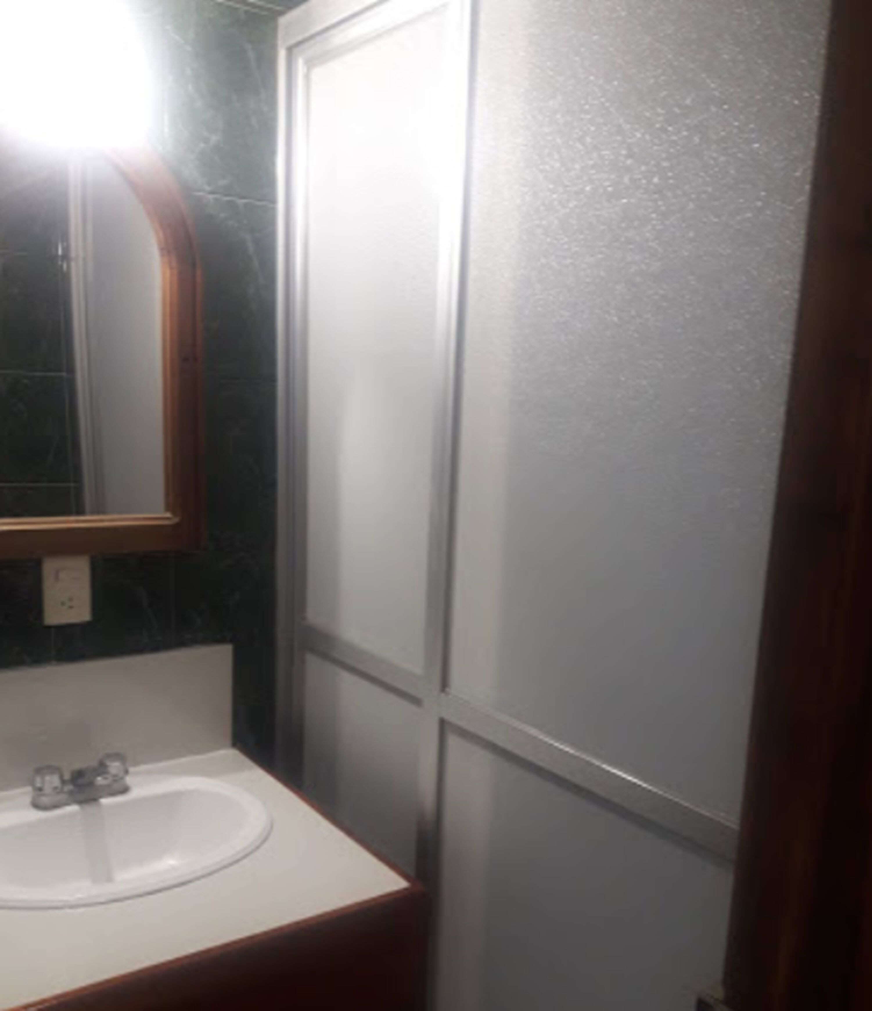A bathroom with a white sink, a mirror with a wooden frame, and a frosted glass partition.