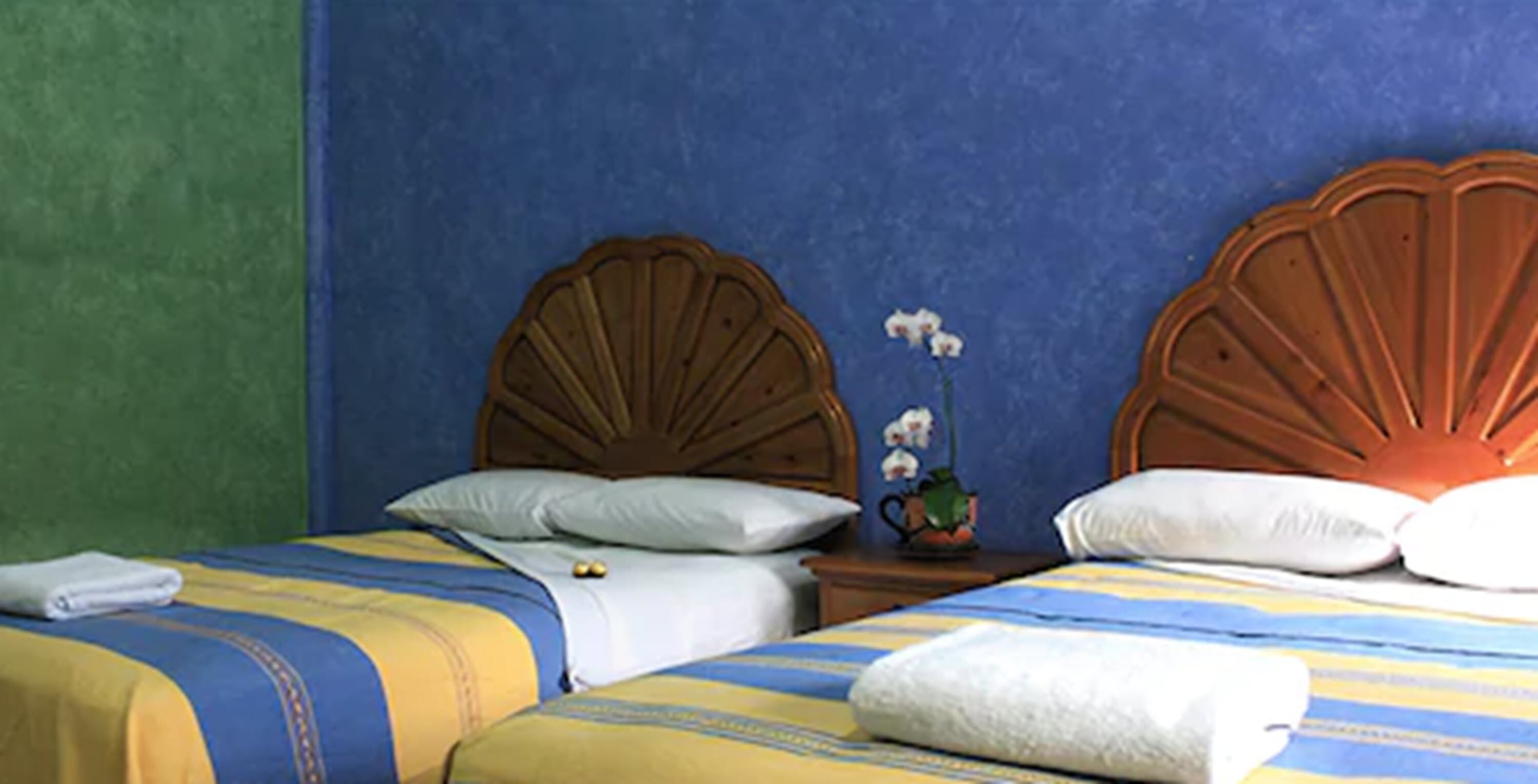 Habitación de hotel con dos camas, cada una con cabecero de madera, almohadas blancas y ropa de cama a rayas.