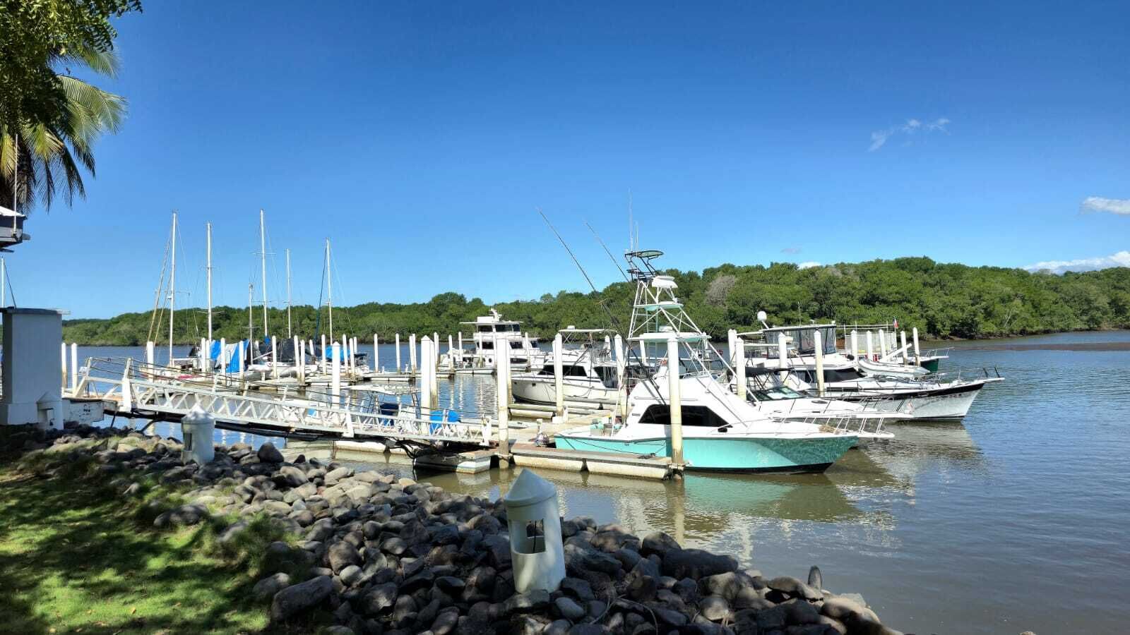 A marina with several boats docked, a rocky shoreline, and a clear blue sky.