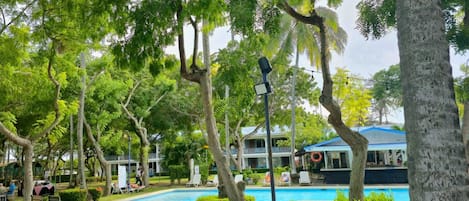 Un área de piscina con sillones reclinables, un flotador salvavidas y un edificio de techo azul al fondo.