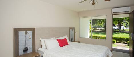 A bedroom with a bed, a nightstand, a ceiling fan, a window with a view of greenery, and an air conditioning unit.