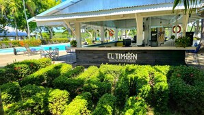 Un restaurante con zona de piscina, mesas al aire libre y abundante vegetación.
