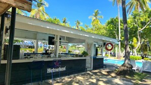 Un bar al aire libre con la marca Heineken, vistas a la piscina, rodeado de palmeras y follaje.