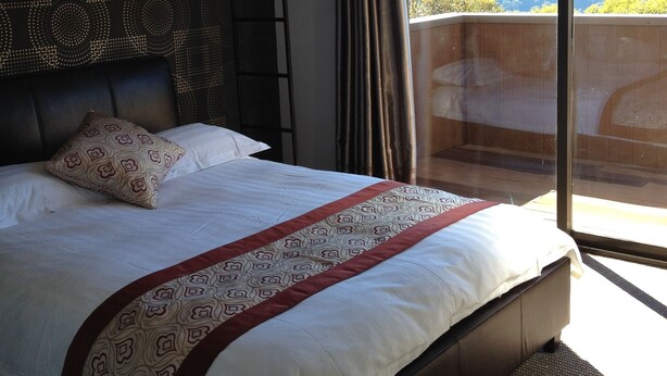 A hotel room with a large bed, a headboard with a patterned design, a window with a view of the outdoors, and a balcony. - Duck Inn Mt Buller (Mount Buller)