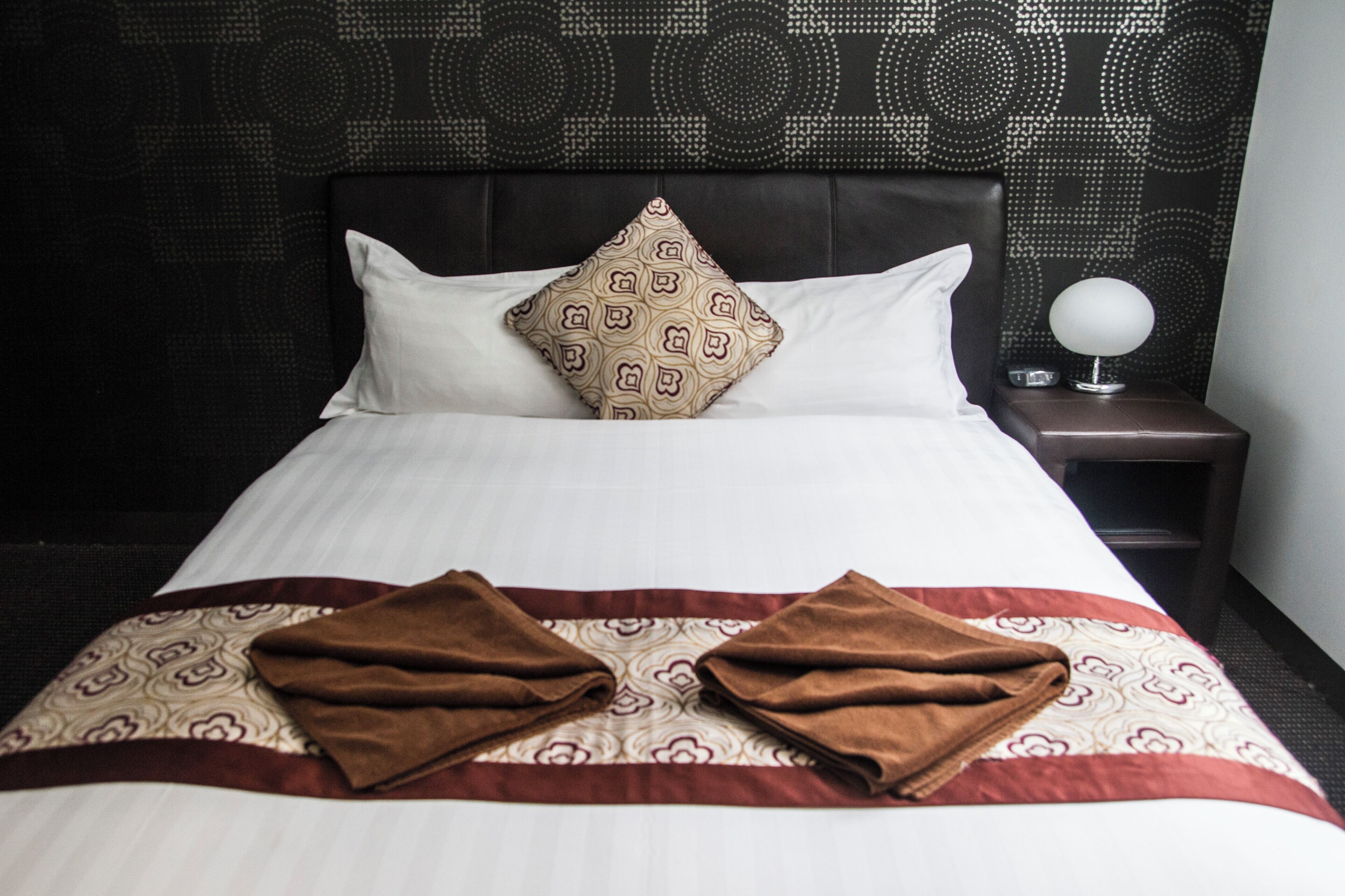 A neatly made bed with a patterned pillow, a decorative headboard, and a bedside table with a lamp.