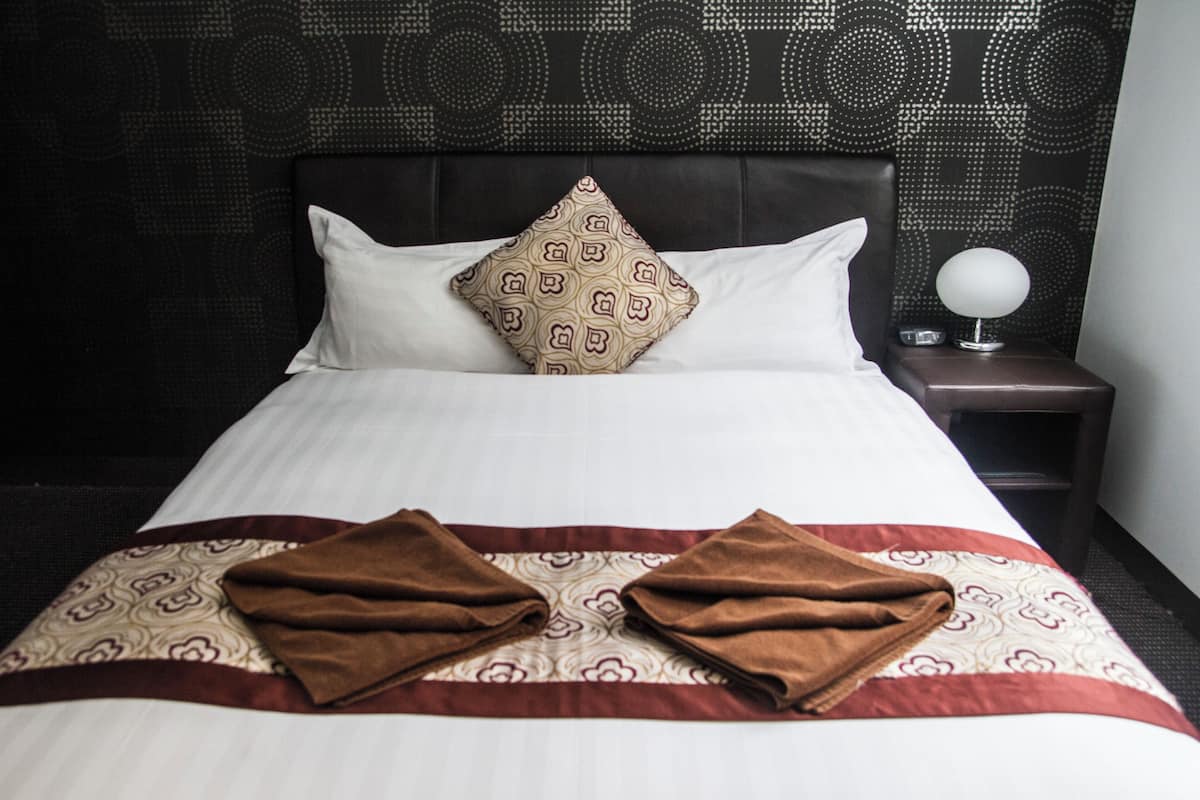 A neatly made bed with a patterned pillow, a decorative headboard, and a bedside table with a lamp.