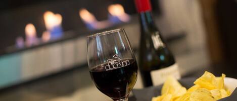 A glass of red wine, a bottle of wine, and a plate of chips on a table with a fireplace in the background.