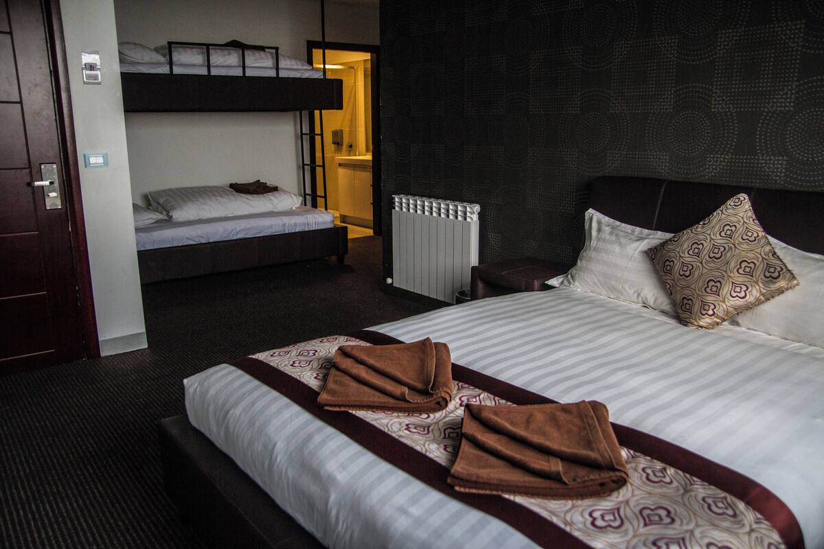 A hotel room with a large bed, a smaller bunk bed, and a radiator.