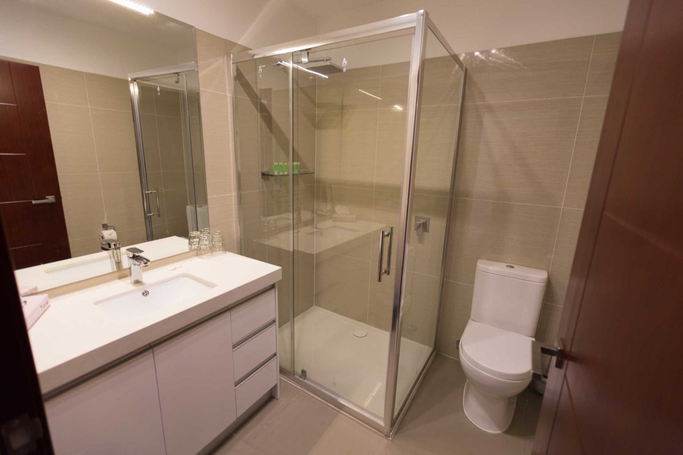 A modern bathroom with a glass-enclosed shower, a white sink with a mirror, and a toilet.