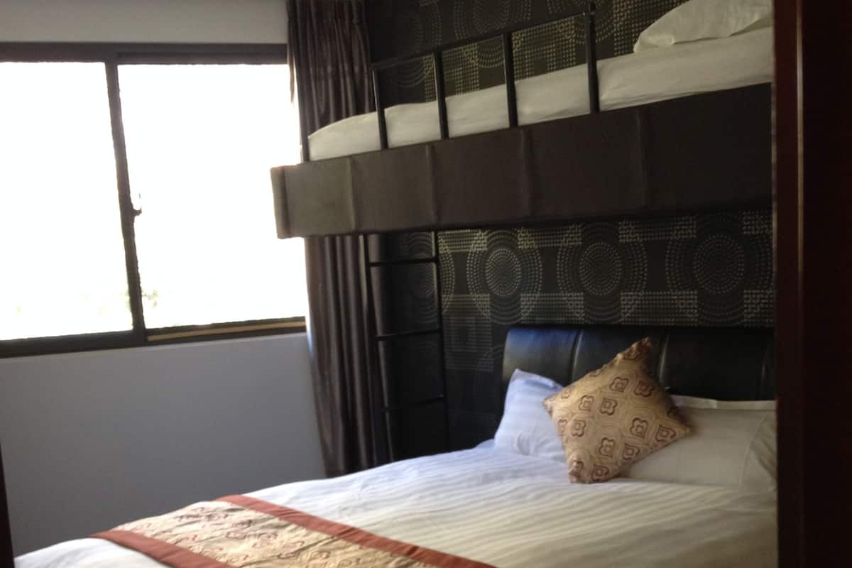 A hotel room with a bunk bed, a patterned headboard, and a large window with curtains.