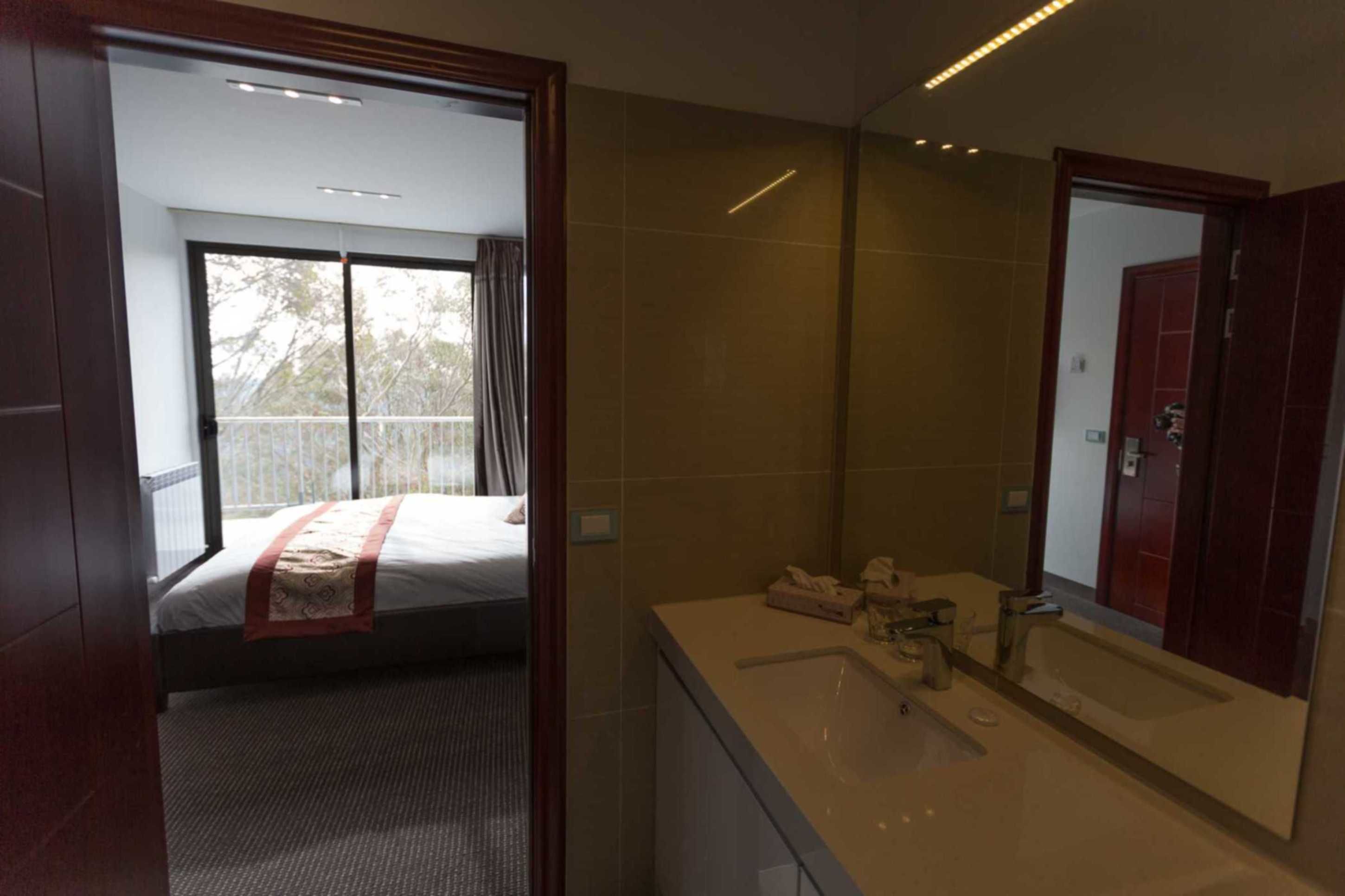 Habitación de hotel con una cama grande, baño con espejo y vista al exterior mediante una puerta corredera.
