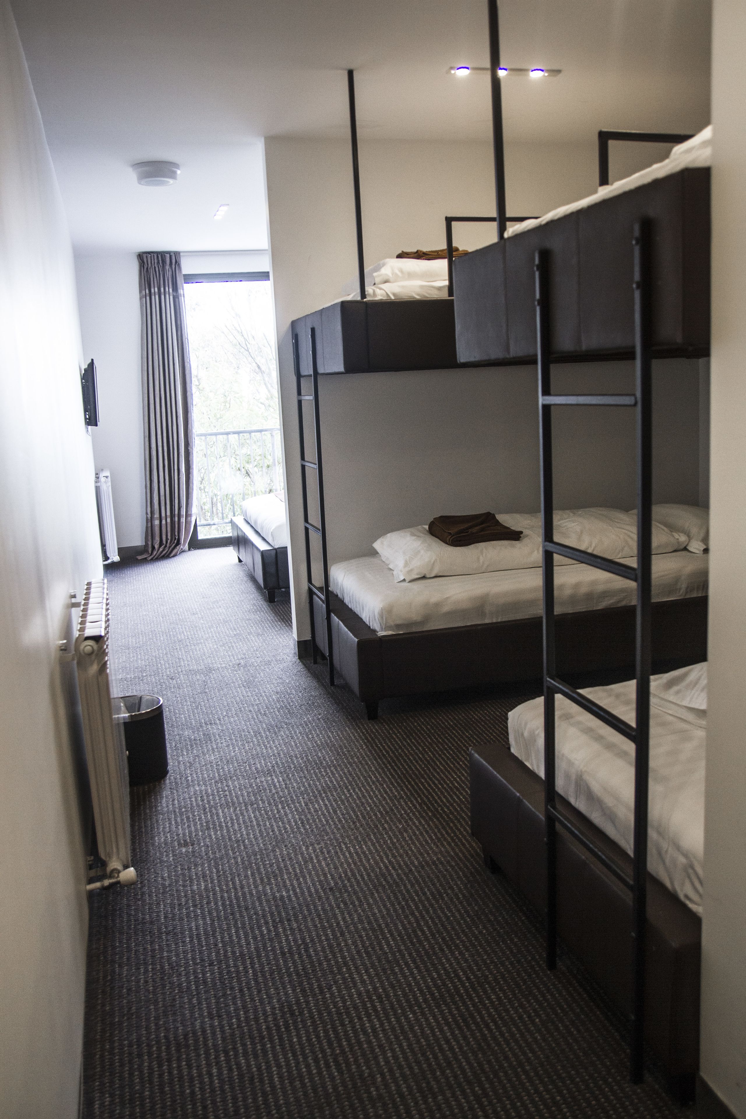A hotel room with bunk beds, a radiator, a window with curtains, and a small table.