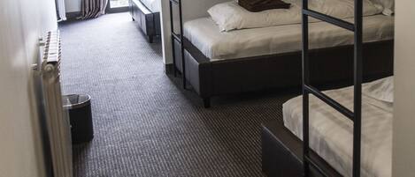 A hotel room with bunk beds, a radiator, a window with curtains, and a small table.