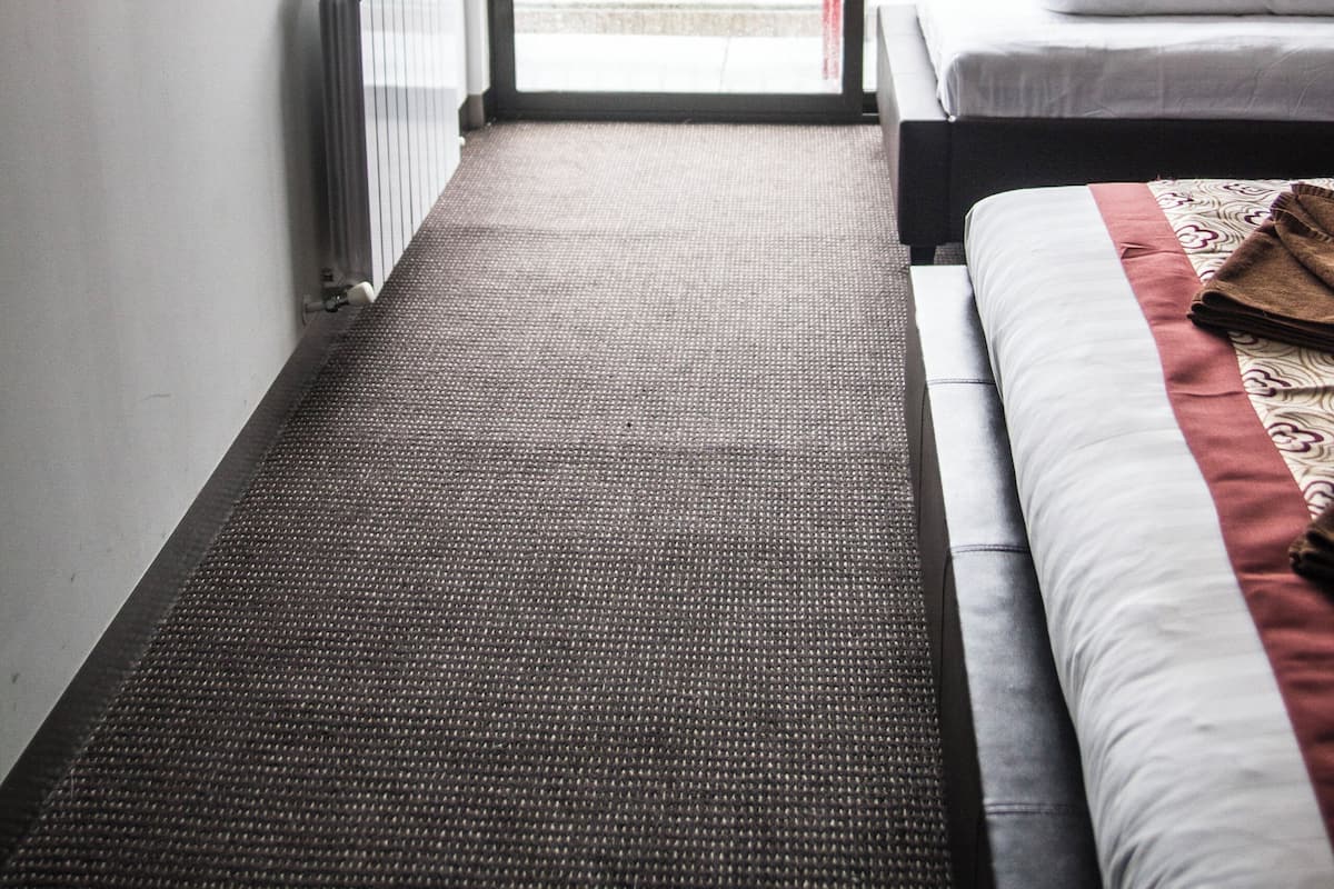 A hotel room with a bed, a TV, a radiator, a sliding glass door to a balcony, and a view of trees outside.