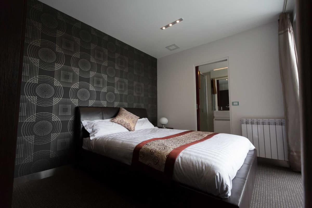 A hotel room with a bed, a patterned wall, a bedside lamp, and a radiator.